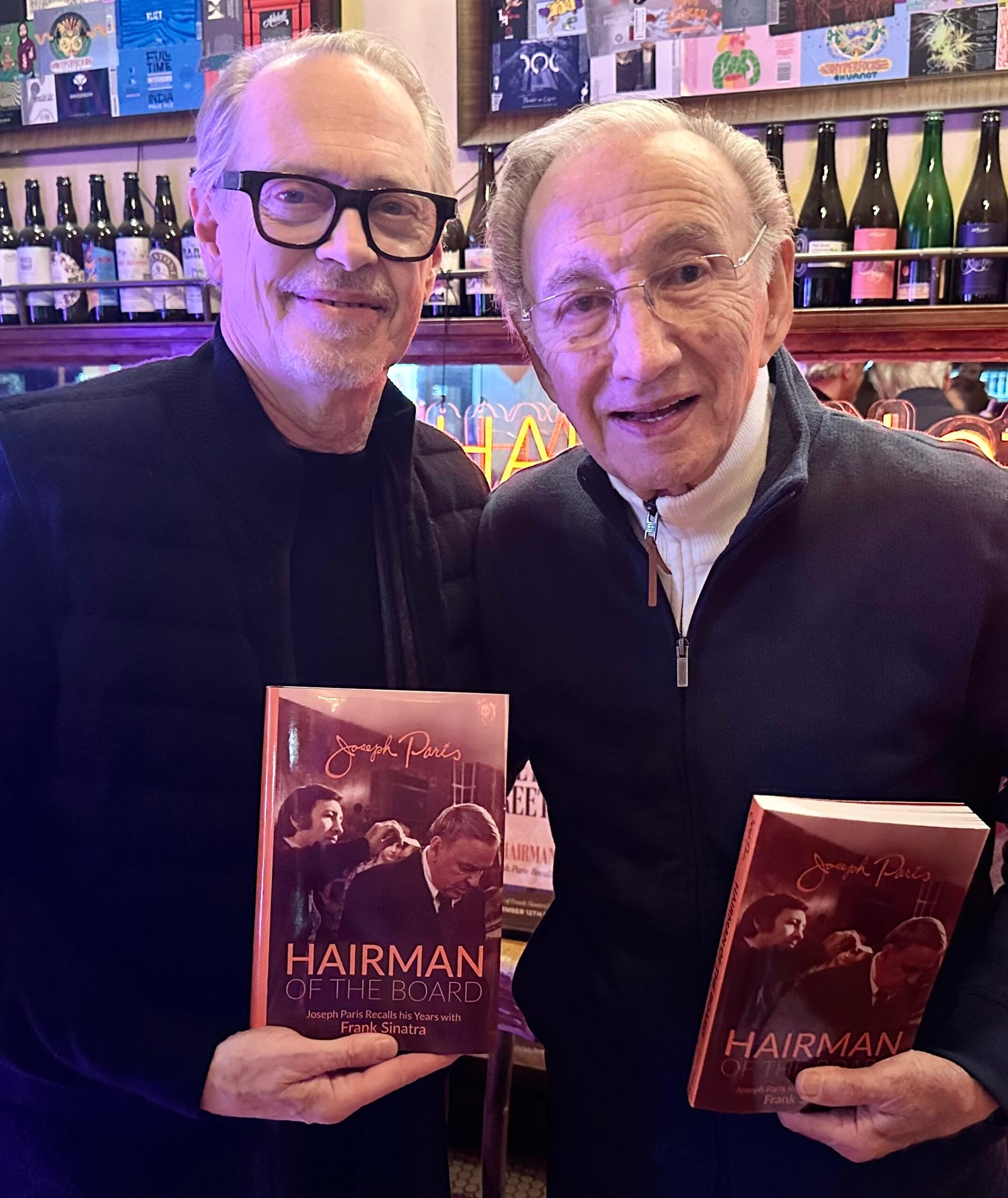 Joseph Paris and Steve Buscemi holding Paris's memoir, celebrating the hairstylist’s legendary career, as featured in The Hair Magazine.