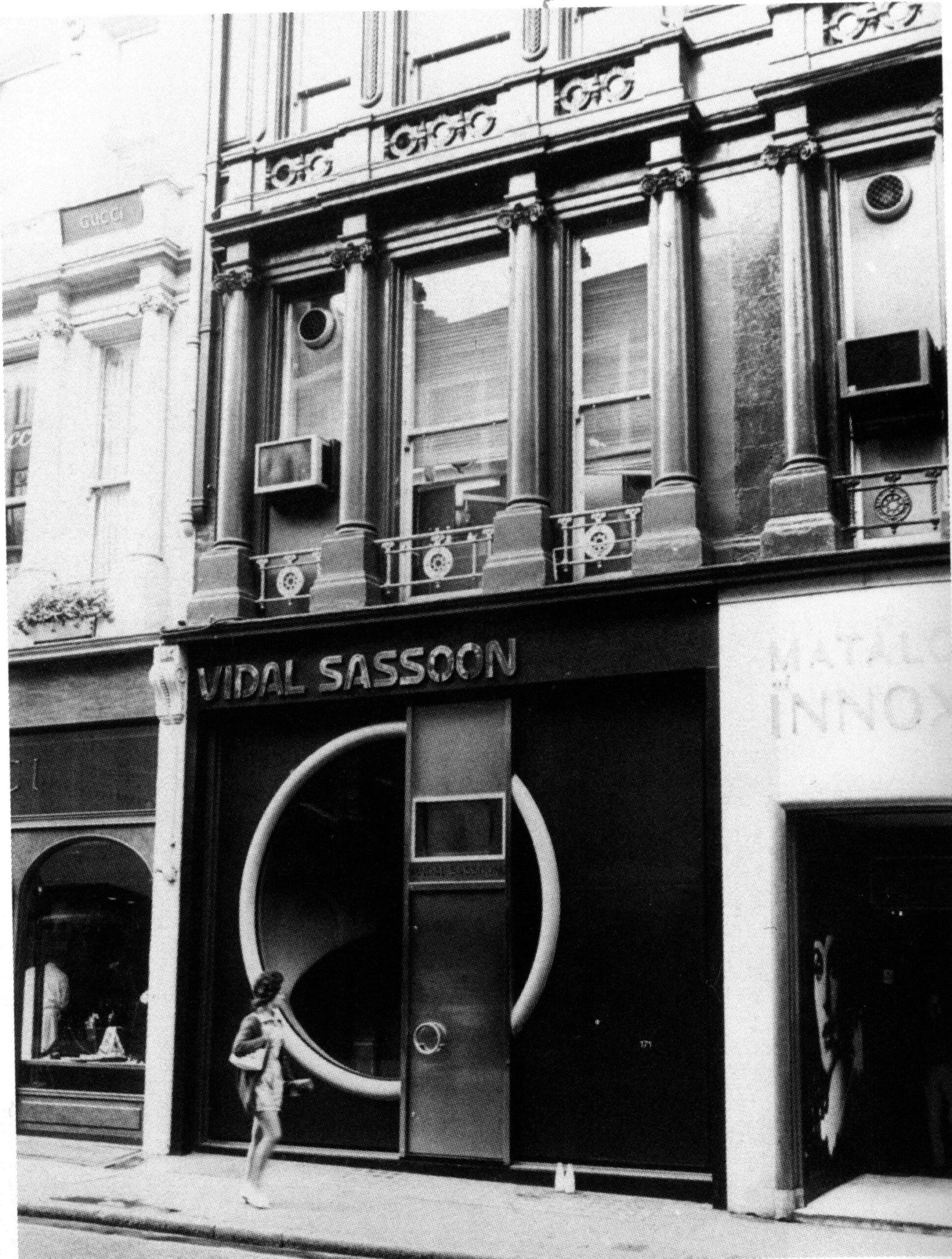 Black and white archive photograph of the Vidal Sassoon salon exterior on Bond Street, London, with the name above the door and a curved graphic in the window.