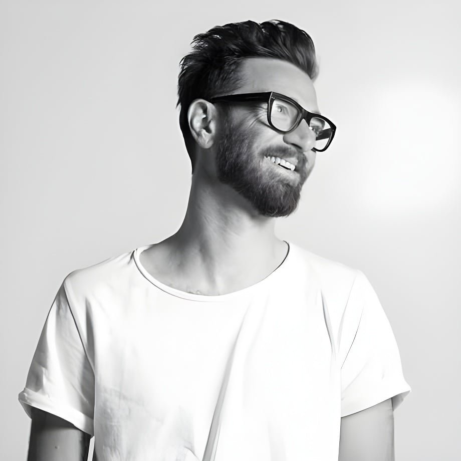 Adam Federico smiling in a black-and-white portrait, short dark hair with volume swept up and back, full beard, thick dark-framed glasses and a white T-shirt Caption: Adam Federico, third-generation member of Sacramento's Federico family of beauty educators.