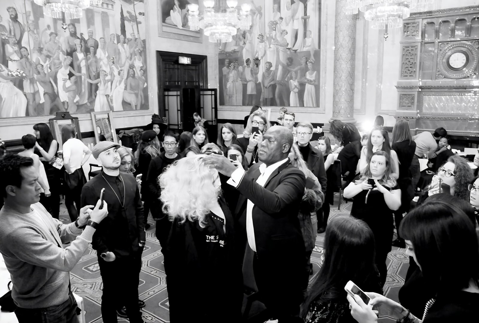 Errol Douglas shapes a model's voluminous, shoulder-length platinum-blonde curls during a live demonstration while hairdressers film on their phones.