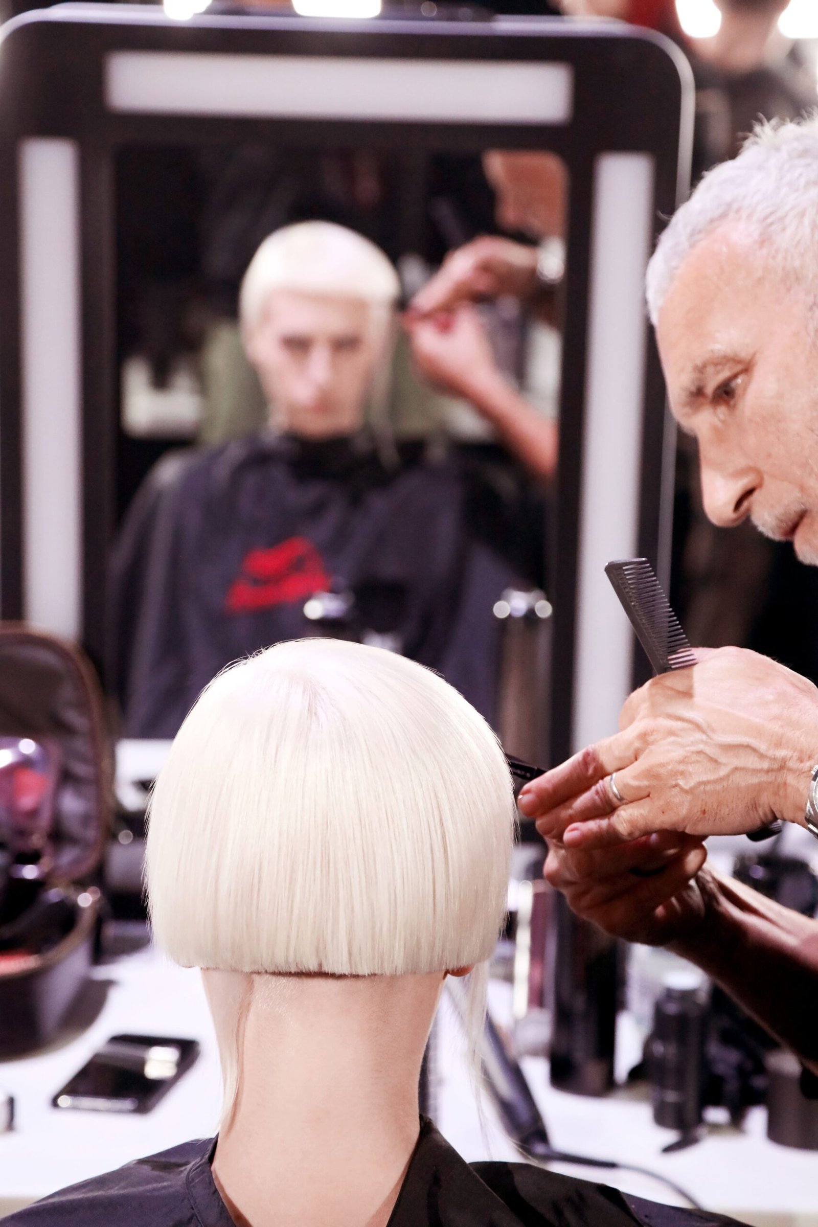 Rounded platinum-blond bob photographed from behind, with a blunt weight line above the nape and a longer disconnected panel falling at the side, sectioned with a comb