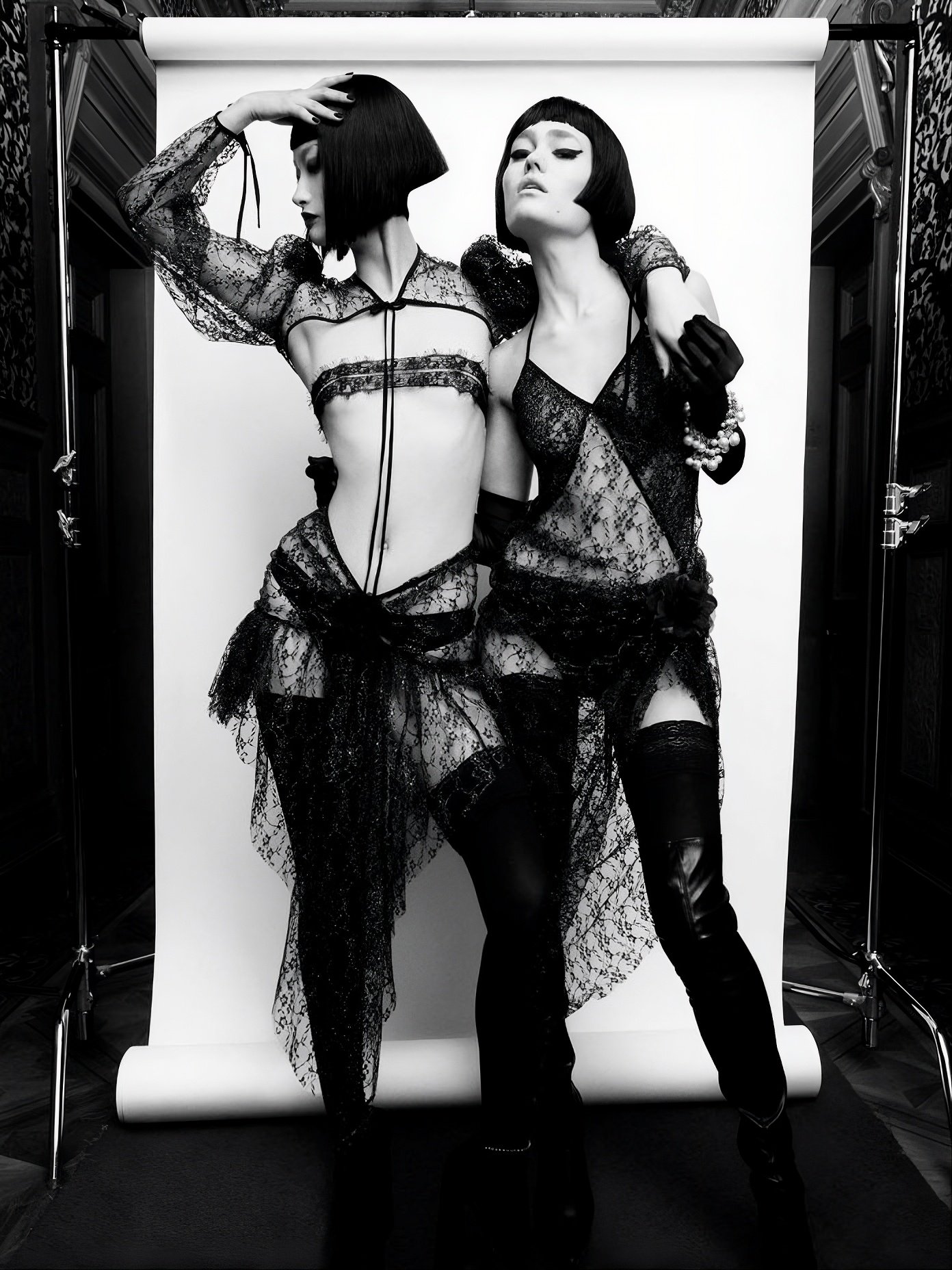 Two models with glossy, blunt black bobs, one jaw-length and angled across the face, the other finished with a very short fringe, posed in black lace against a white paper backdrop.