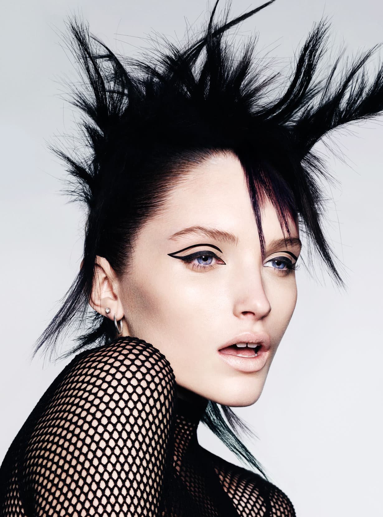 Model with jet-black hair set in sharp upward spikes, sleek sides, a long swept fringe streaked with plum, and graphic double-winged black eyeliner.