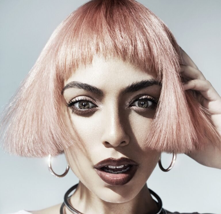 Model with a chin-length pastel pink bob, blunt heavy bangs and high-shine finish, bronze eye makeup and a deep brown lip